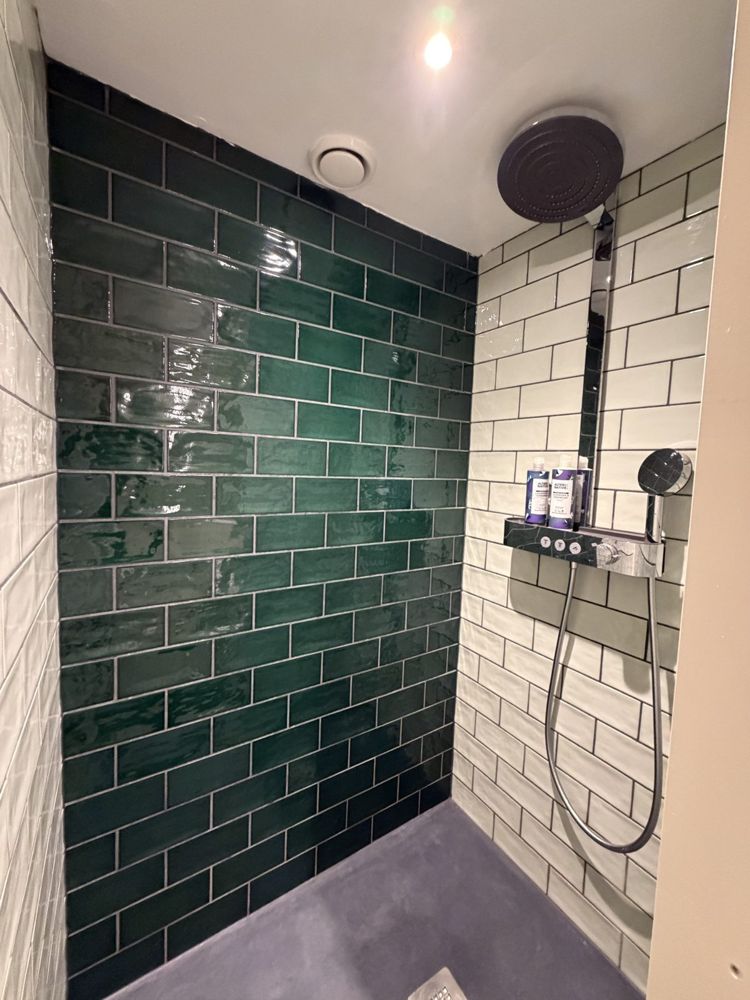 A walk-in shower with dark green tiles and a rainfall head